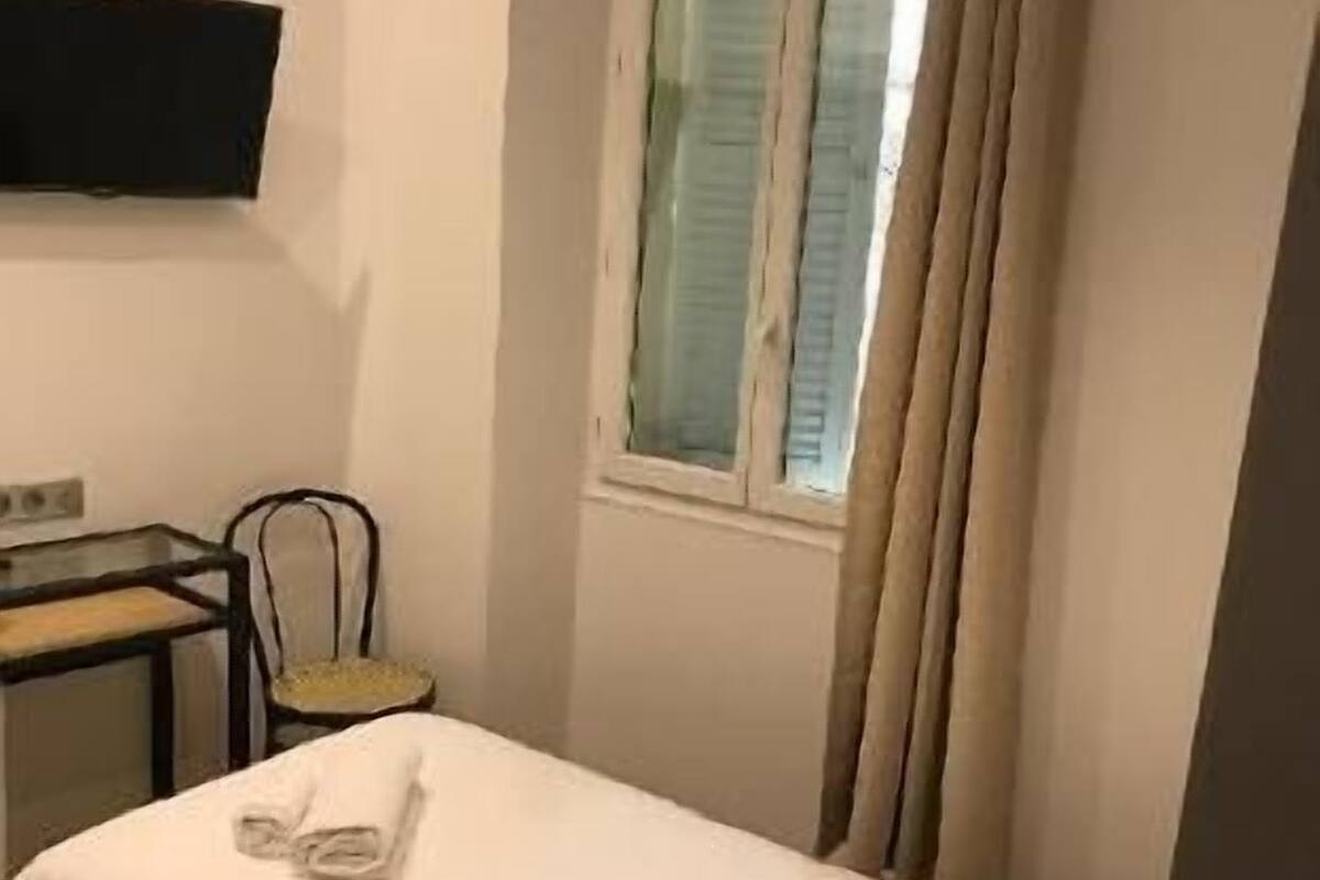 A small, single-bed room with a desk, chair, and a TV mounted on the wall.