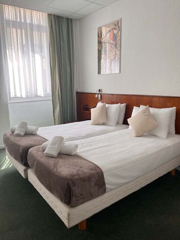 Una cama doble con ropa de cama blanca y marrón, un cabecero y una mesita de noche con una lámpara.