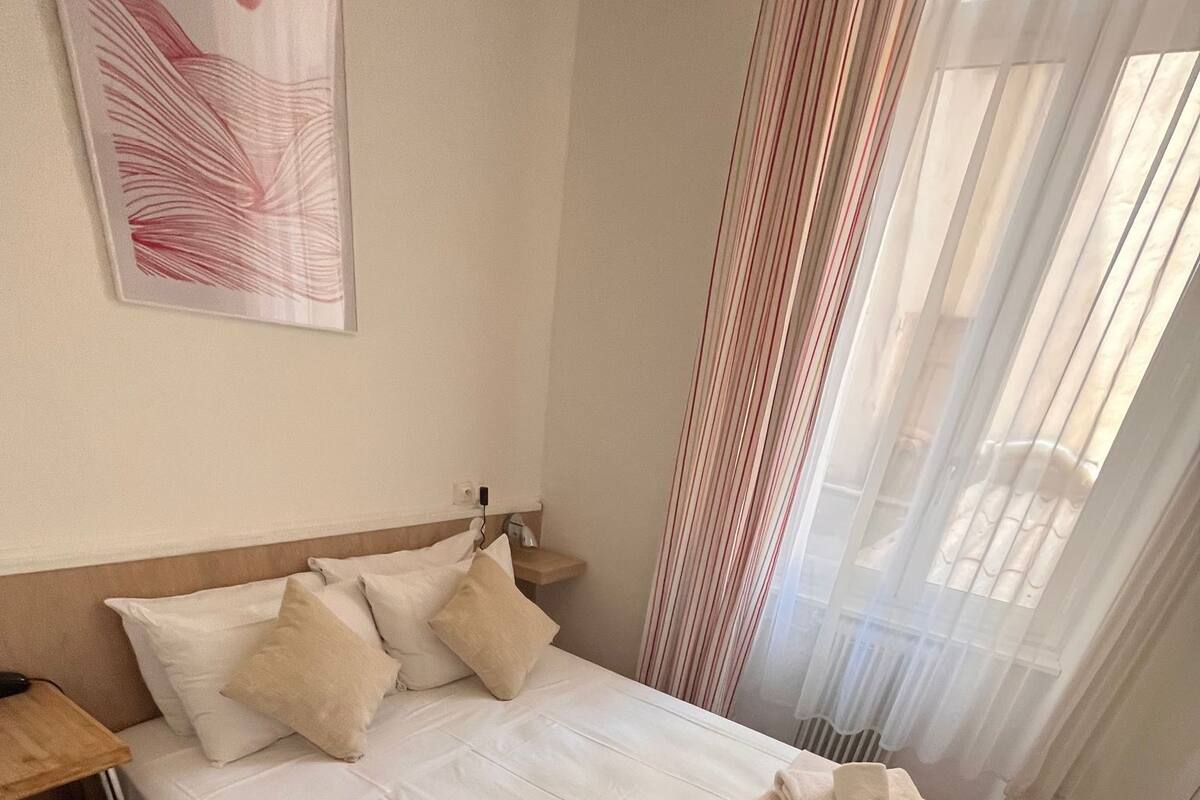 Una habitación de hotel con cama, almohadas, una mesita de noche, un escritorio y una silla.
