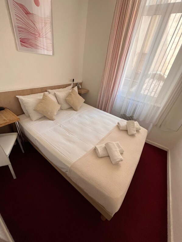 Una habitación de hotel con cama, almohadas, una mesita de noche, un escritorio y una silla.