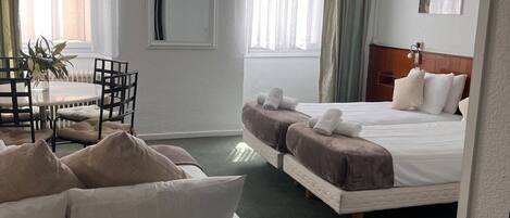 A hotel room with a bed, a sofa, a dining table with chairs, and a window with curtains.