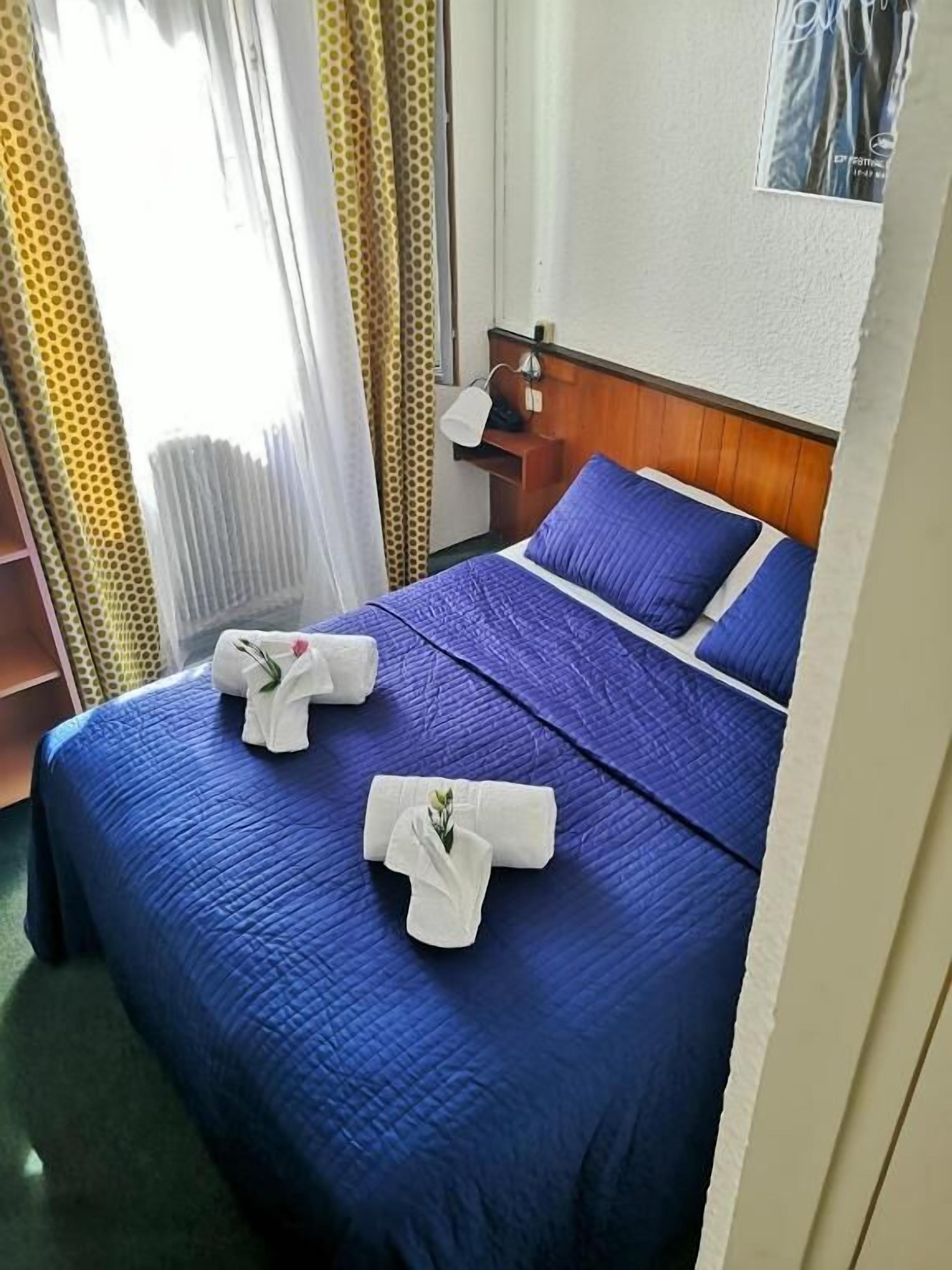 A hotel room with a bed, a nightstand, and a window with curtains.