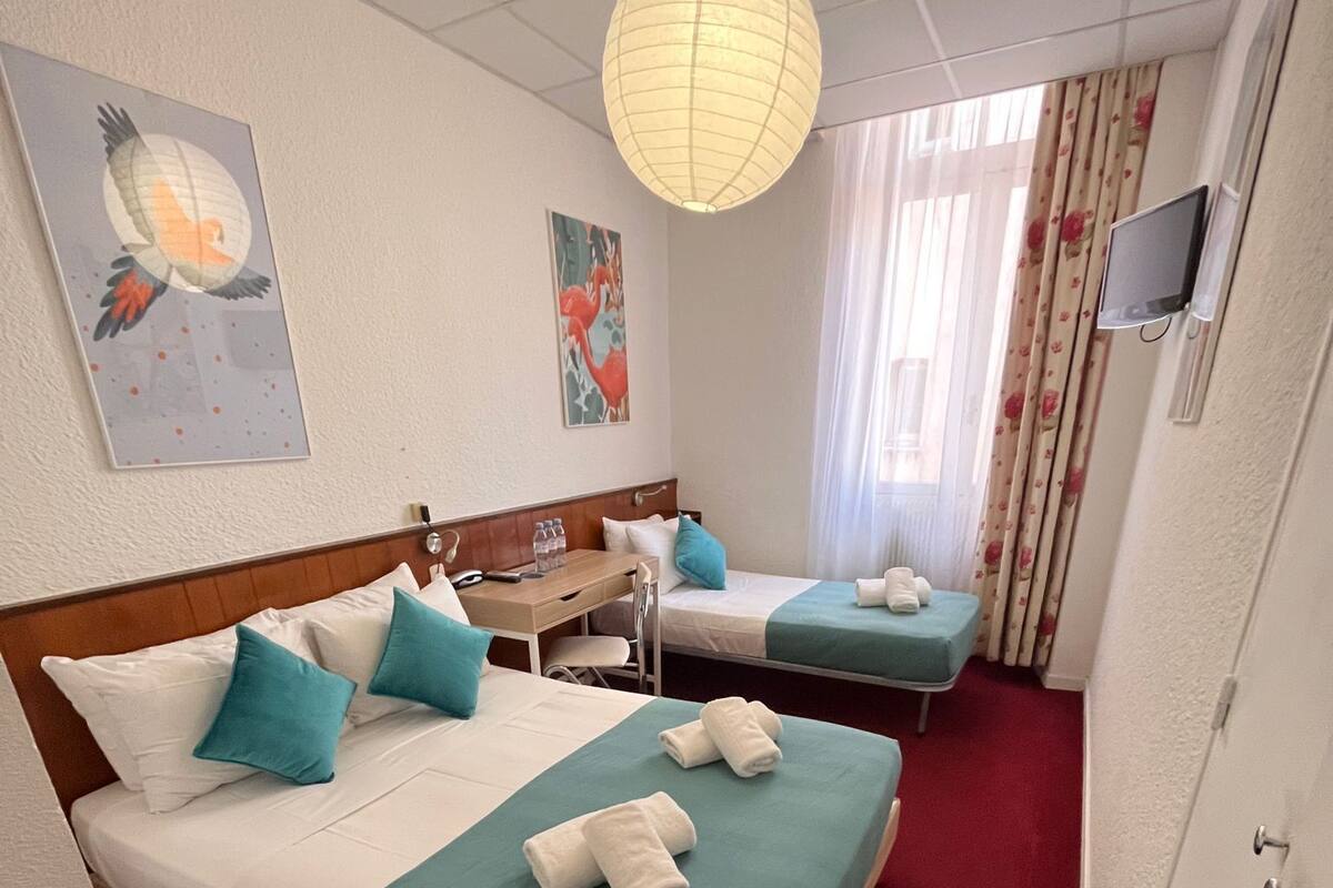 Habitación de hotel con dos camas, un escritorio, una silla, un televisor y obras de arte en las paredes.