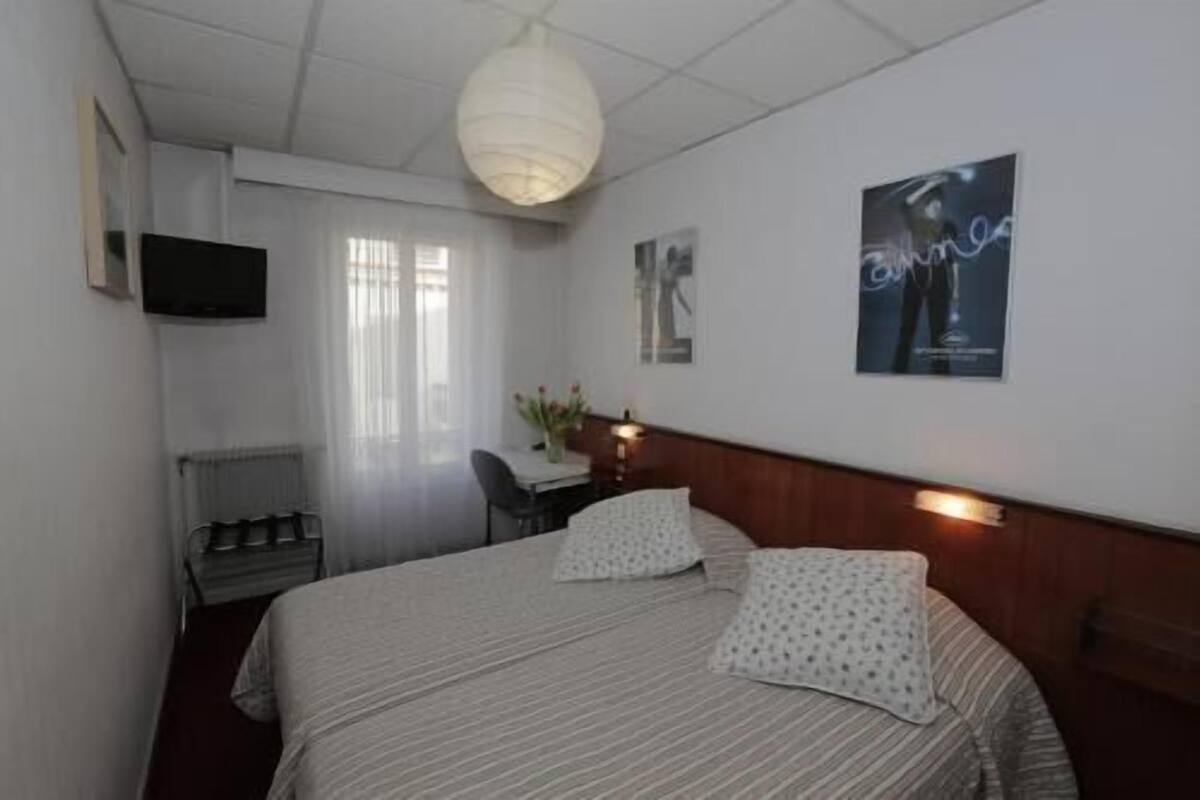 Habitación de hotel con cama, escritorio, silla, televisor y un cartel en la pared.