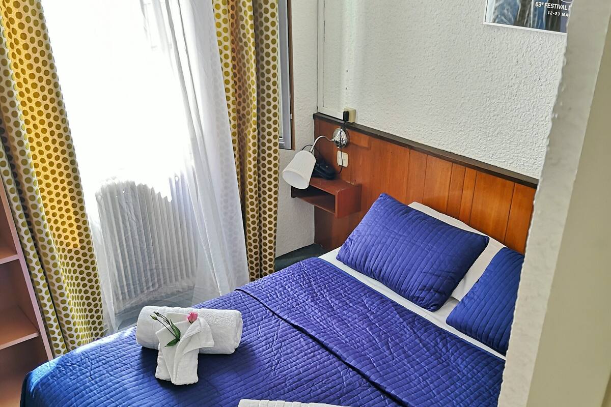 Una habitación de hotel con cama, mesita de noche, lámpara y cortinas.