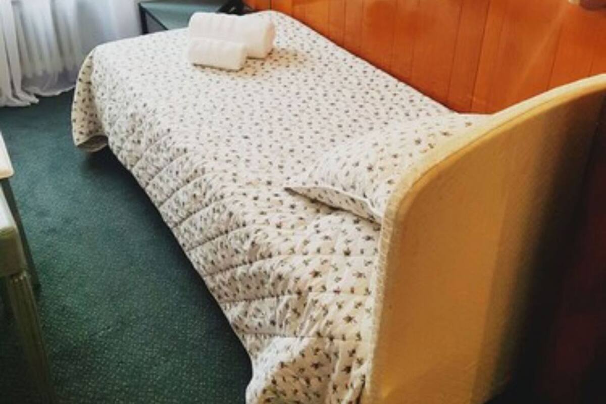 Una cama individual con colcha estampada de flores, cabecera de madera y mesita de noche con lámpara.