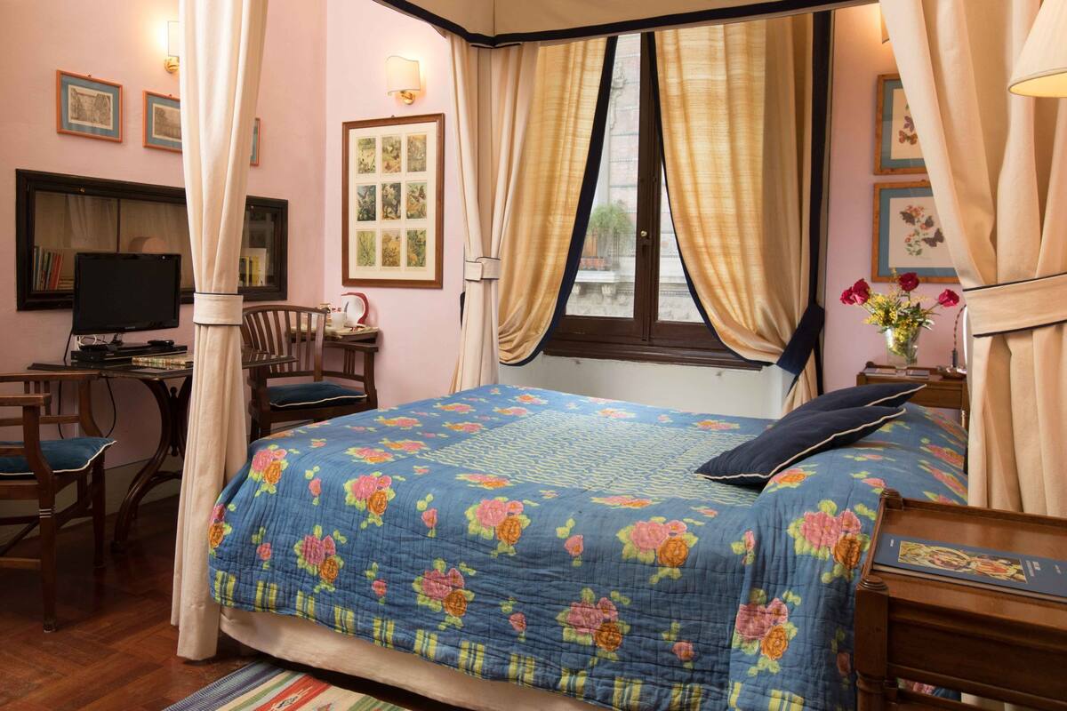 A bedroom with a four-poster bed, a desk with a computer, and a chair.