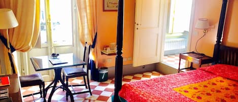 Una habitación de hotel con piso a cuadros, una cama con dosel, un escritorio con silla y una ventana con cortinas.
