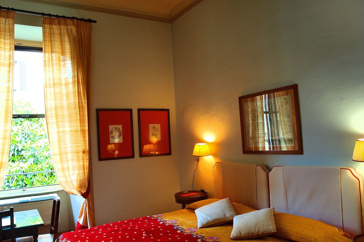 A hotel room with a bed, two bedside lamps, a framed picture on the wall, and a window with curtains.