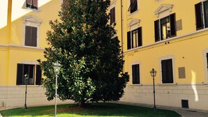 A courtyard with a large tree, a street lamp, and a yellow building with multiple windows and shutters. - Residenza Johanna I (Florence)
