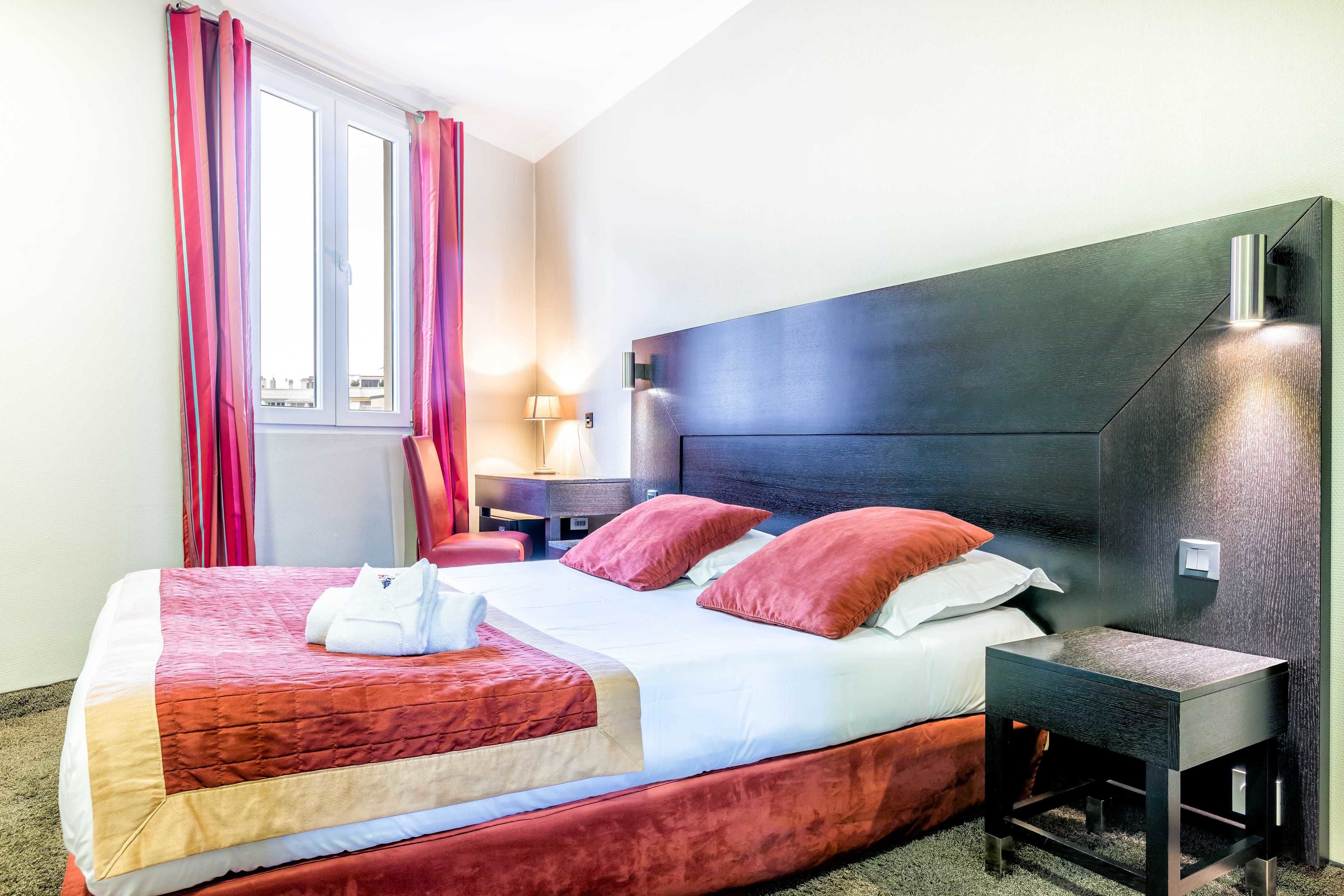 A hotel room with a large bed, a bedside table, a nightstand, and a window with curtains.