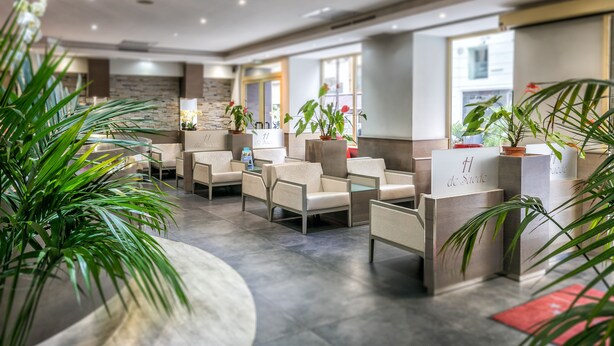 A modern hotel lobby with seating areas, potted plants, and a stone accent wall.