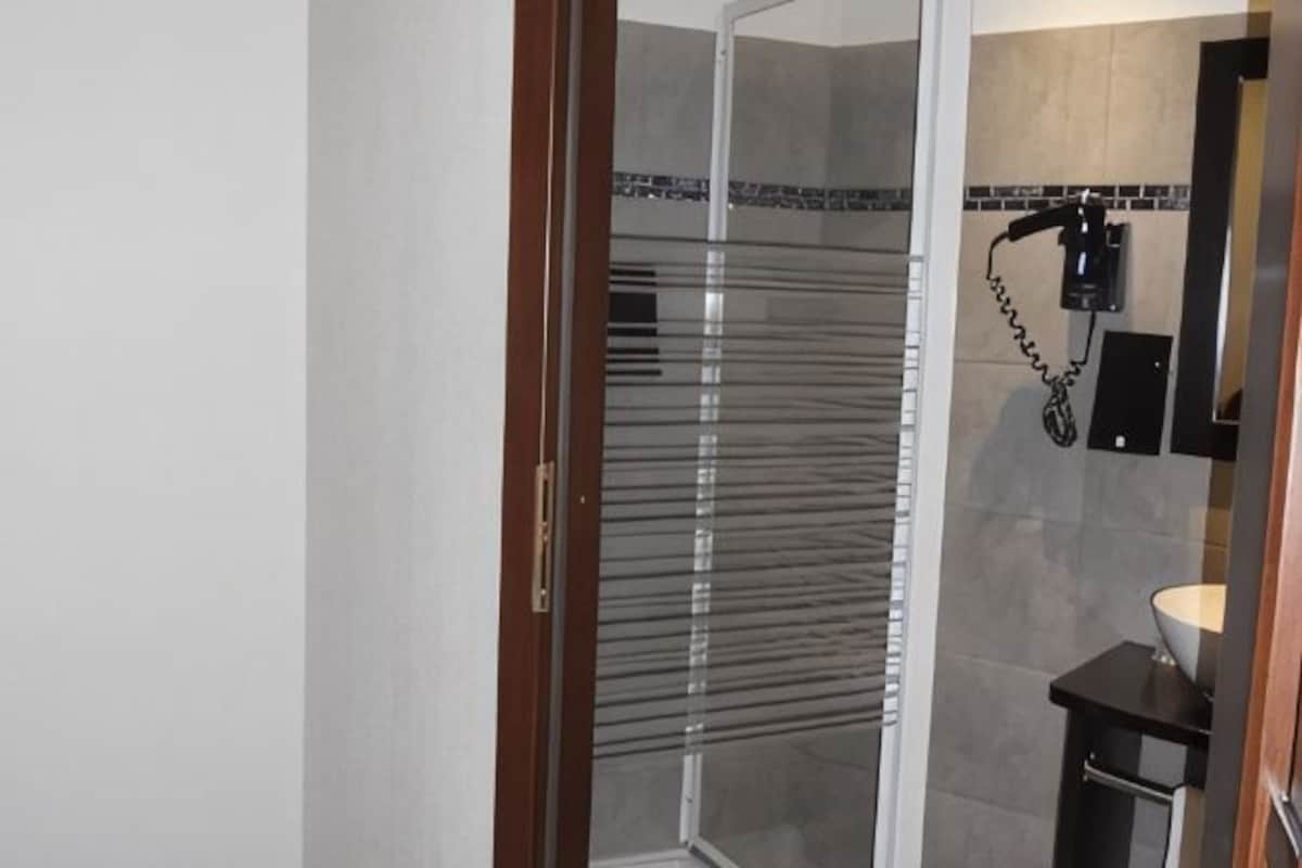 A glass-enclosed shower area with a towel rack and a wall-mounted hairdryer.