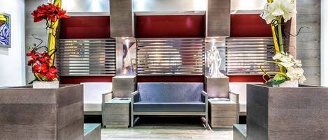 A modern reception area with a sofa, two side tables, and decorative plants.