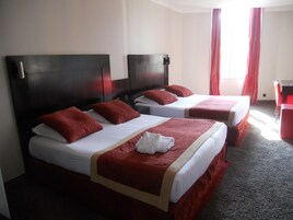 Una camera d'albergo con due letti, ognuno con lenzuola rosse e biancheria bianca, una testiera in legno e una sedia rossa.