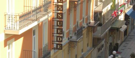 A hotel with balconies, a sign reading "HOTEL SUEDES", and a street with a motorbike.