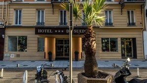 A multi-story hotel with balconies, a palm tree in the foreground, and a sign reading "HOTEL *** D".