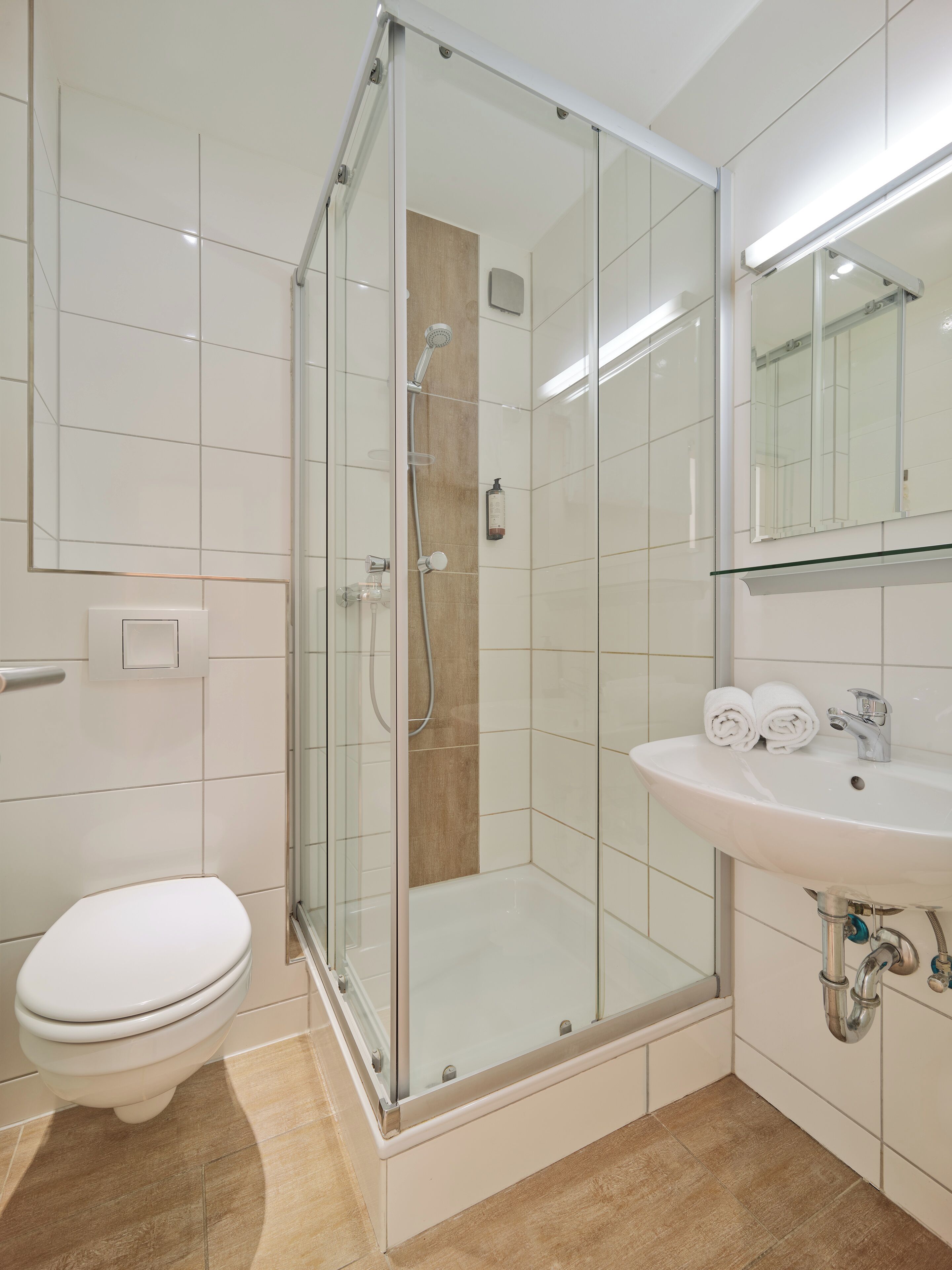 A bathroom with a glass-enclosed shower, a white toilet, and a sink with towels.