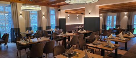 Un restaurant avec des tables et des chaises en bois, des lustres et de grandes fenêtres.