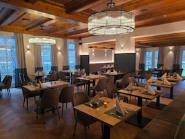 A restaurant with wooden tables and chairs, chandeliers, and large windows.