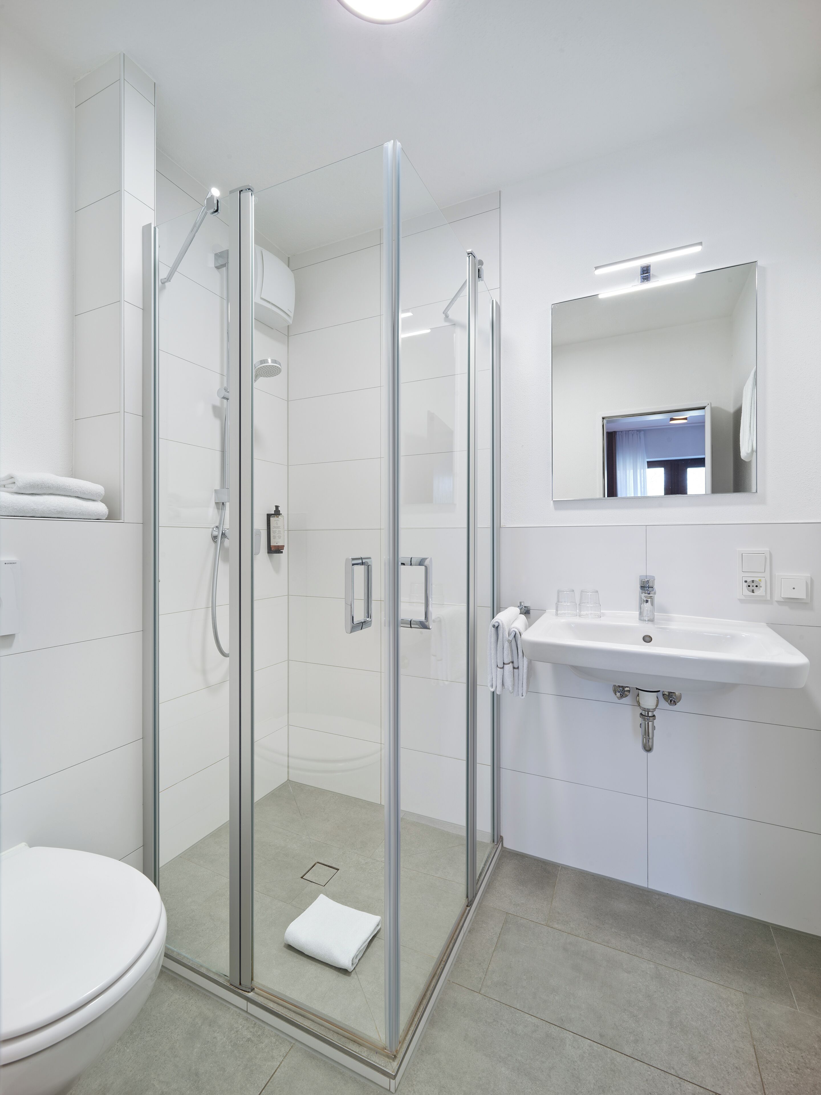 Ein modernes Badezimmer mit einer Duschkabine, einem weißen Waschbecken und einer Toilette.