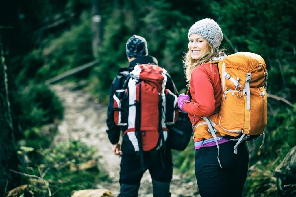 Two people hiking on a forest trail with backpacks.
