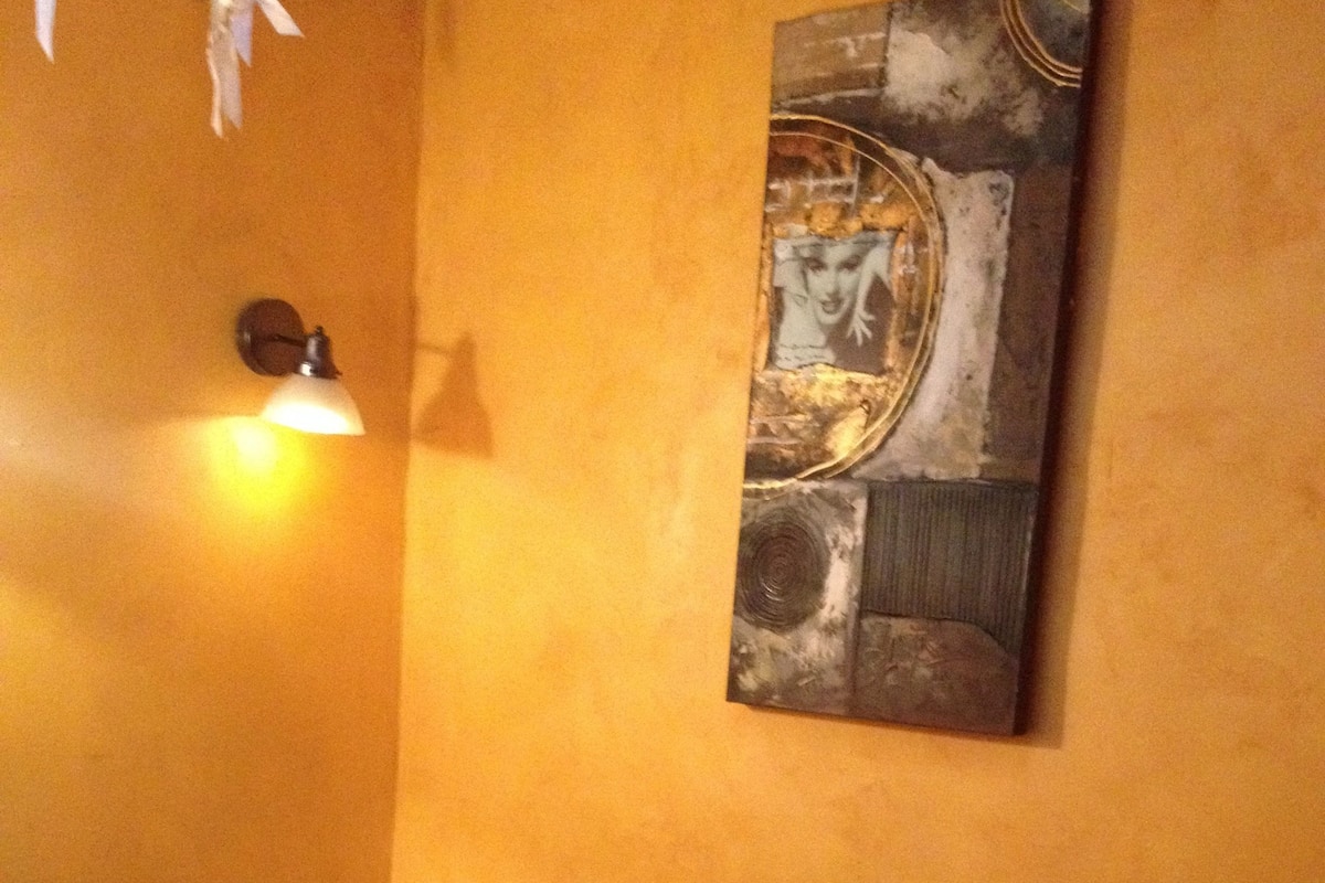A room with a purple bed, a wall-mounted abstract painting, and a wall-mounted light fixture.