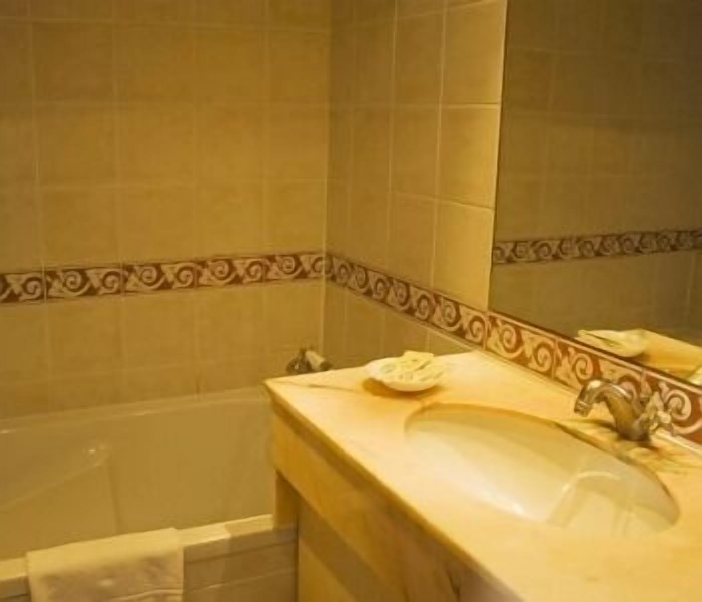 Un baño con un lavamanos color crema, un espejo y azulejos decorativos en la pared.