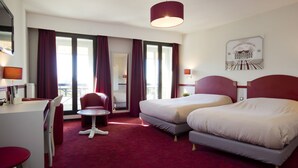 A hotel room with two beds, a desk, a chair, a table, and a view of the city. - Hôtel des 4 Soeurs (Bordeaux)