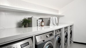 A modern laundry room with a marble countertop, two front-loading washing machines, a drying rack, and a plant. - Bob W Munich Schwabing (Munich)