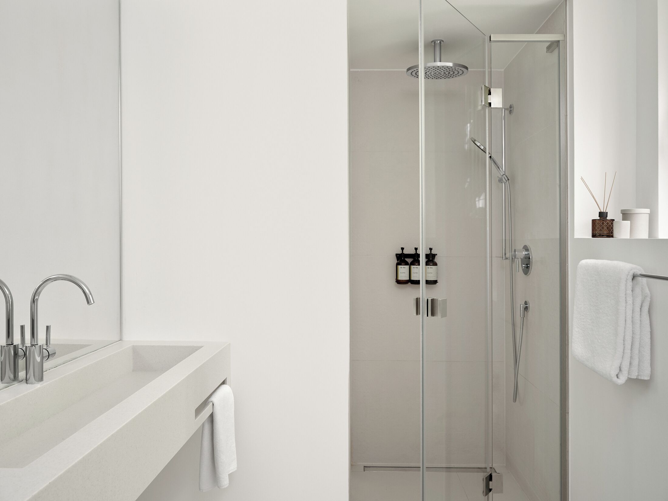 A modern bathroom with a glass-enclosed shower, a white sink with two faucets, and a towel hanging on the wall.