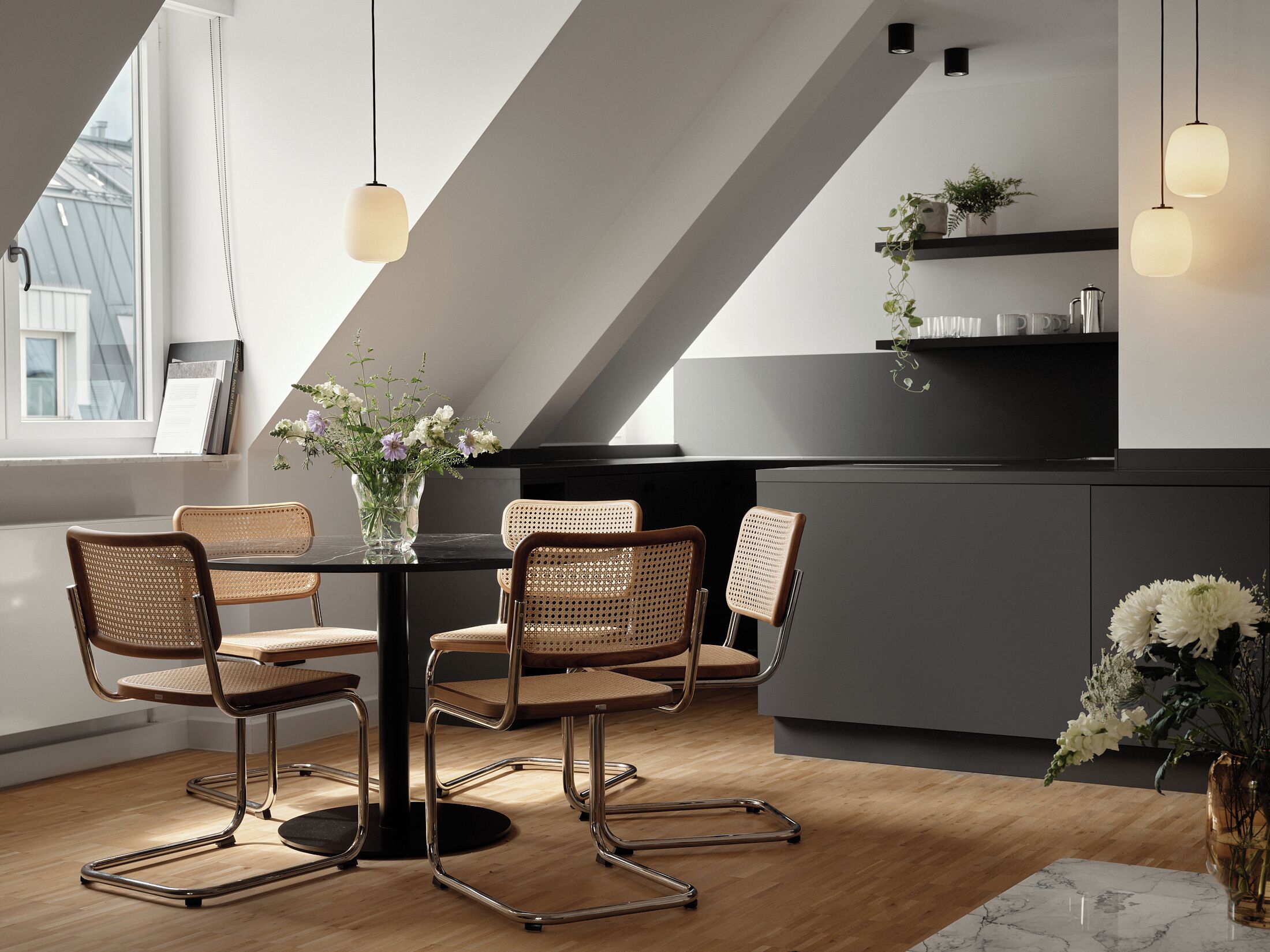 Una cocina moderna con comedor, que incluye una mesa de comedor negra con cuatro sillas de mimbre, una isla negra e iluminación colgante.