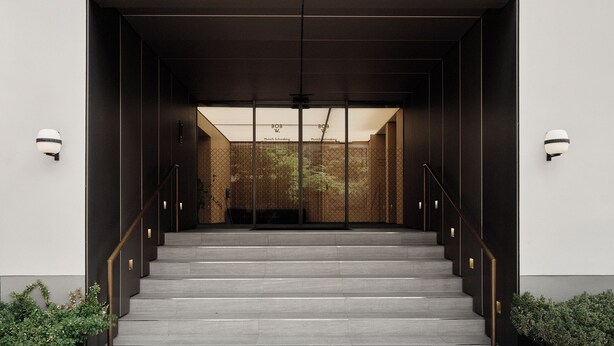 A modern building entrance with a staircase leading to a glass door, metal railings, and two wall-mounted light fixtures. - Bob W Munich Schwabing (Munich)