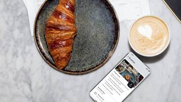 Un croissant sobre un plato, una taza de café y un menú en la mesa.