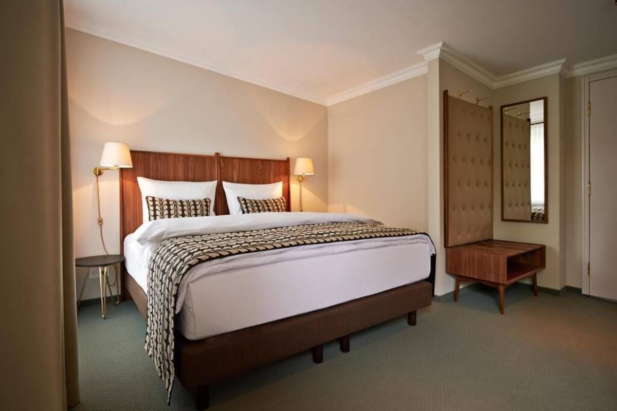 Habitació d'hotel amb un llit gran, dues làmpades de nit, una tauleta de nit de fusta i un mirall.