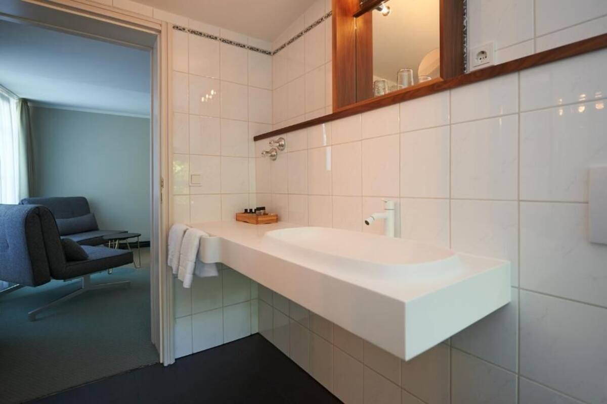 Un bany modern amb un lavabo blanc, un mirall i una dutxa.