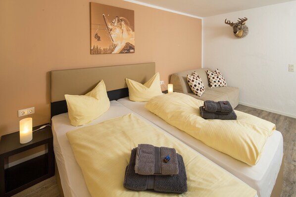 Habitación de hotel con dos camas, cada una con ropa y almohadas amarillas, un cabecero, una mesita de noche con lámpara y un adorno de cabeza de ciervo fijado a la pared.