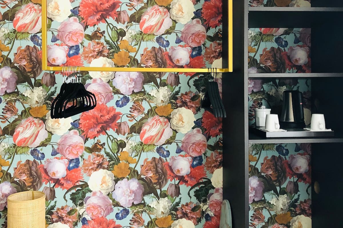Una habitación con papel tapiz floral, una estantería negra y un bolso negro colgando.