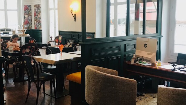 A restaurant with wooden tables and chairs, a large window, and a wall-mounted light fixture. - AMA Hôtel (Biarritz)