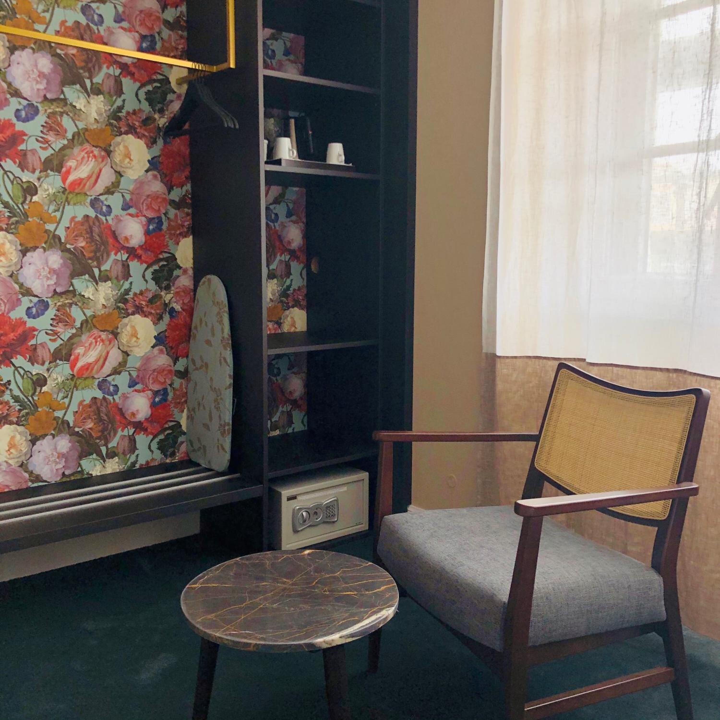 Una habitación con papel tapiz floral, una mesa redonda, una silla y una estantería.