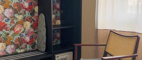 Una habitación con papel tapiz floral, una mesa redonda, una silla y una estantería.