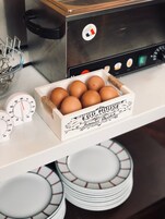Una cocina con un electrodoméstico de acero inoxidable, una caja blanca con la etiqueta 'EGG HOUSE' que contiene huevos, y una balanza.