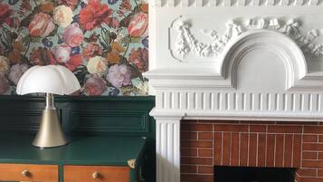 Una habitación con un aparador verde, una chimenea blanca con marco de ladrillo y un papel tapiz floral.
