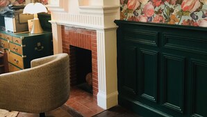 A room with a fireplace, floral wallpaper, a round mirror, and a wooden floor. - AMA Hôtel (Biarritz)