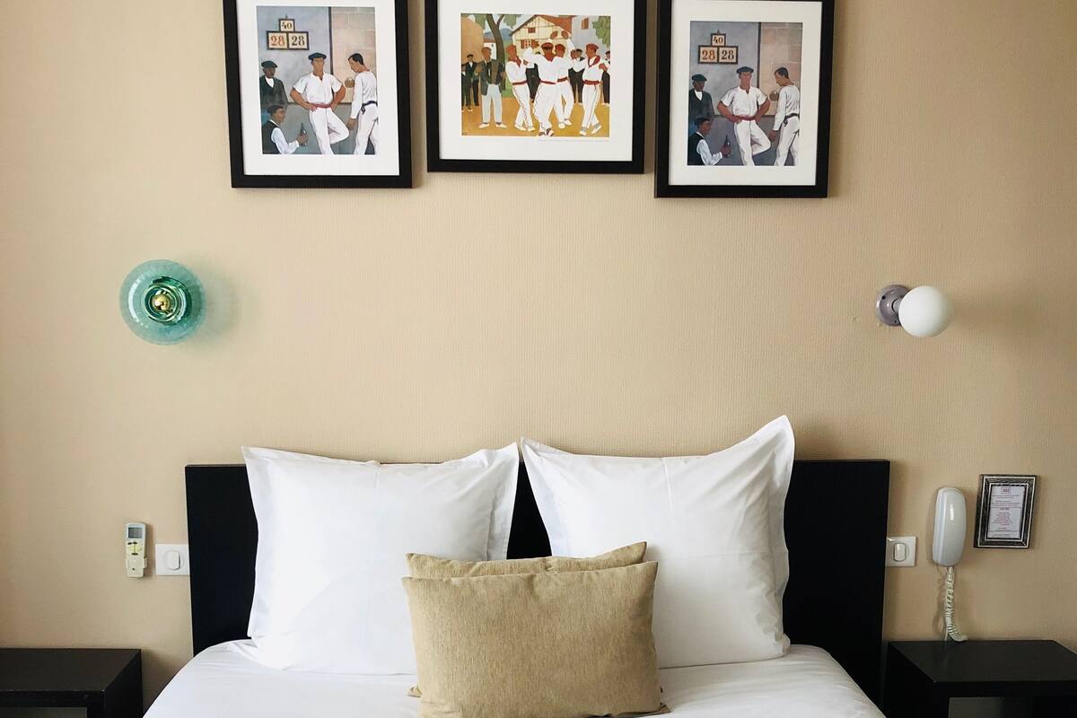 Habitación de hotel con una cama grande, dos mesitas de noche, un teléfono en la pared y tres cuadros enmarcados sobre la cama.