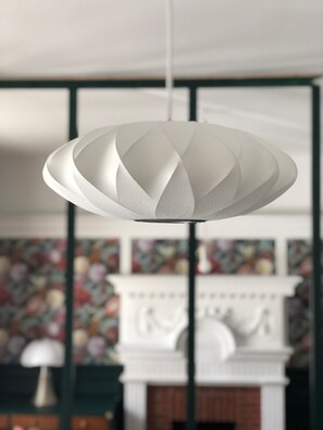 A modern pendant light fixture with a geometric design, hanging in a room with a fireplace and patterned wallpaper. - AMA Hôtel (Biarritz)