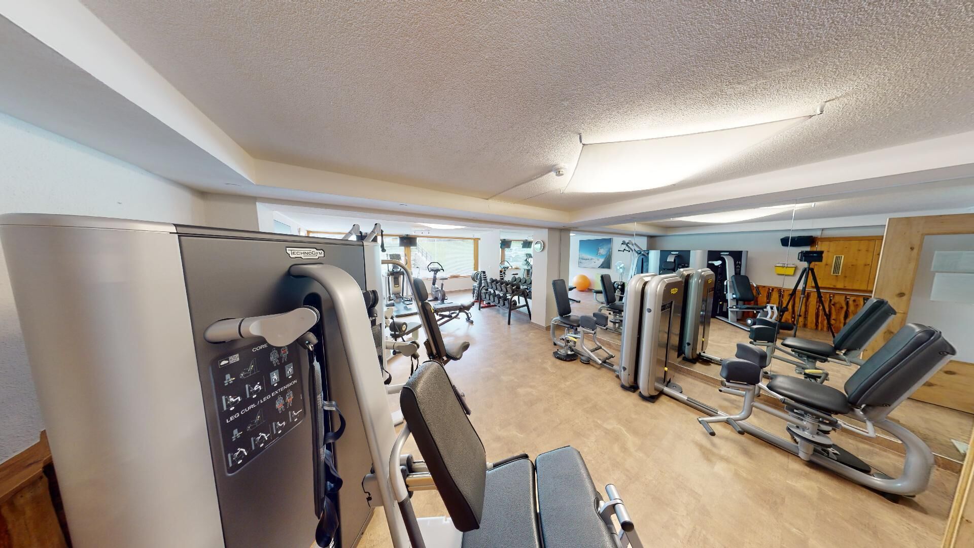 Un gimnasio con varios equipos de ejercicio, como una máquina para curl de piernas, mancuernas y bancos de pesas.