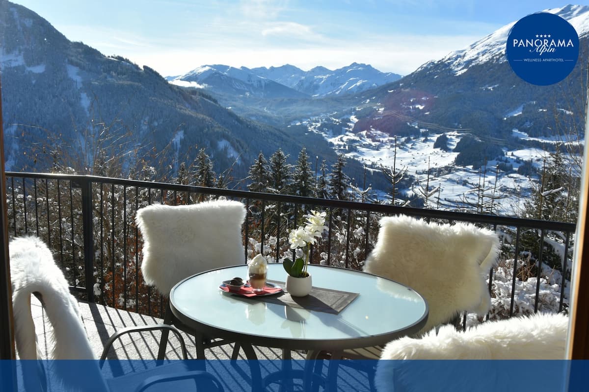 Un balcon avec une table en verre, deux chaises blanches, une petite plante en pot et un verre contenant une boisson.