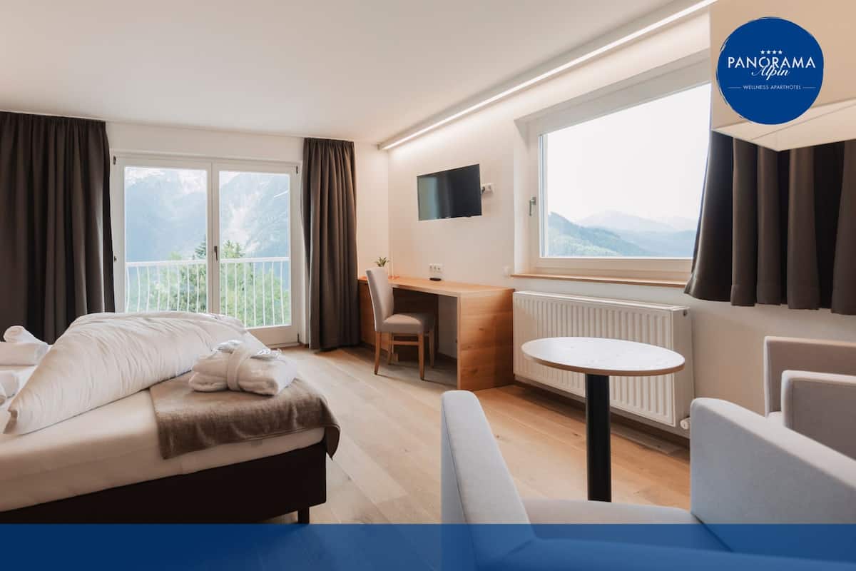 Une chambre d’hôtel moderne équipée d’un lit, d’un bureau, d’une chaise, d’une table ronde et offrant une vue sur les montagnes.