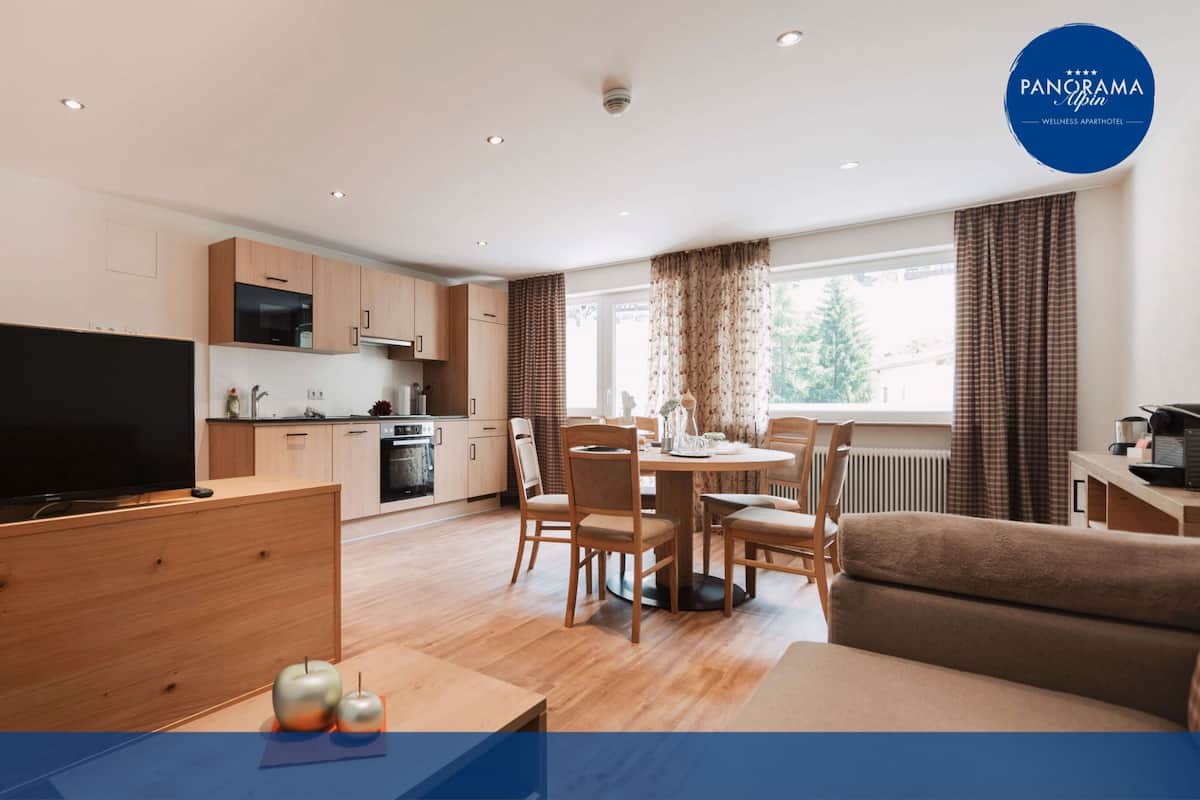 Un appartement moderne doté d’un téléviseur à écran plat, de meubles en bois, d’un coin repas et d’une cuisine.